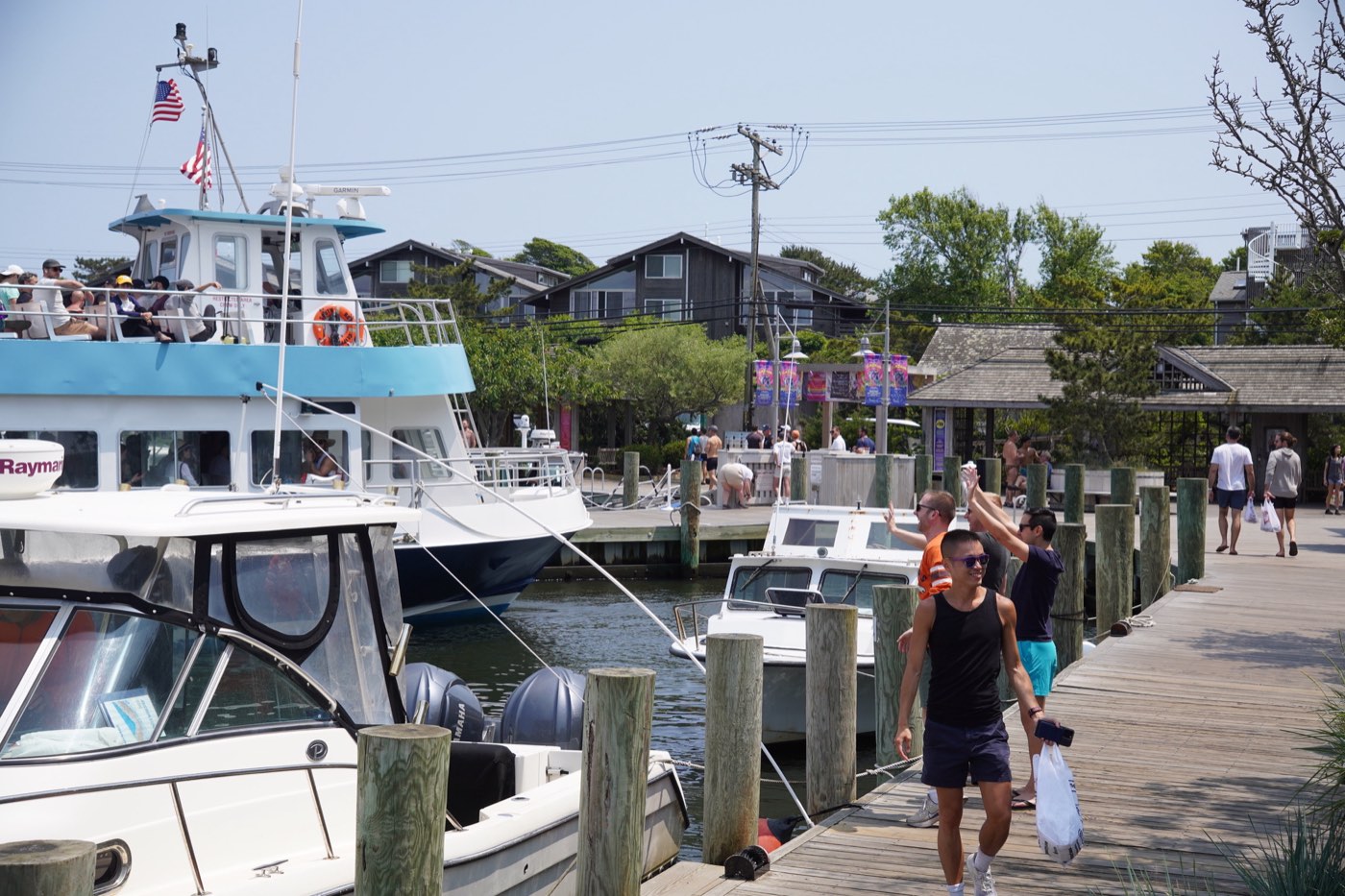 The Sayville ferry docked at Fire Island Pines harbor, guests walking the boardwalk with bags.