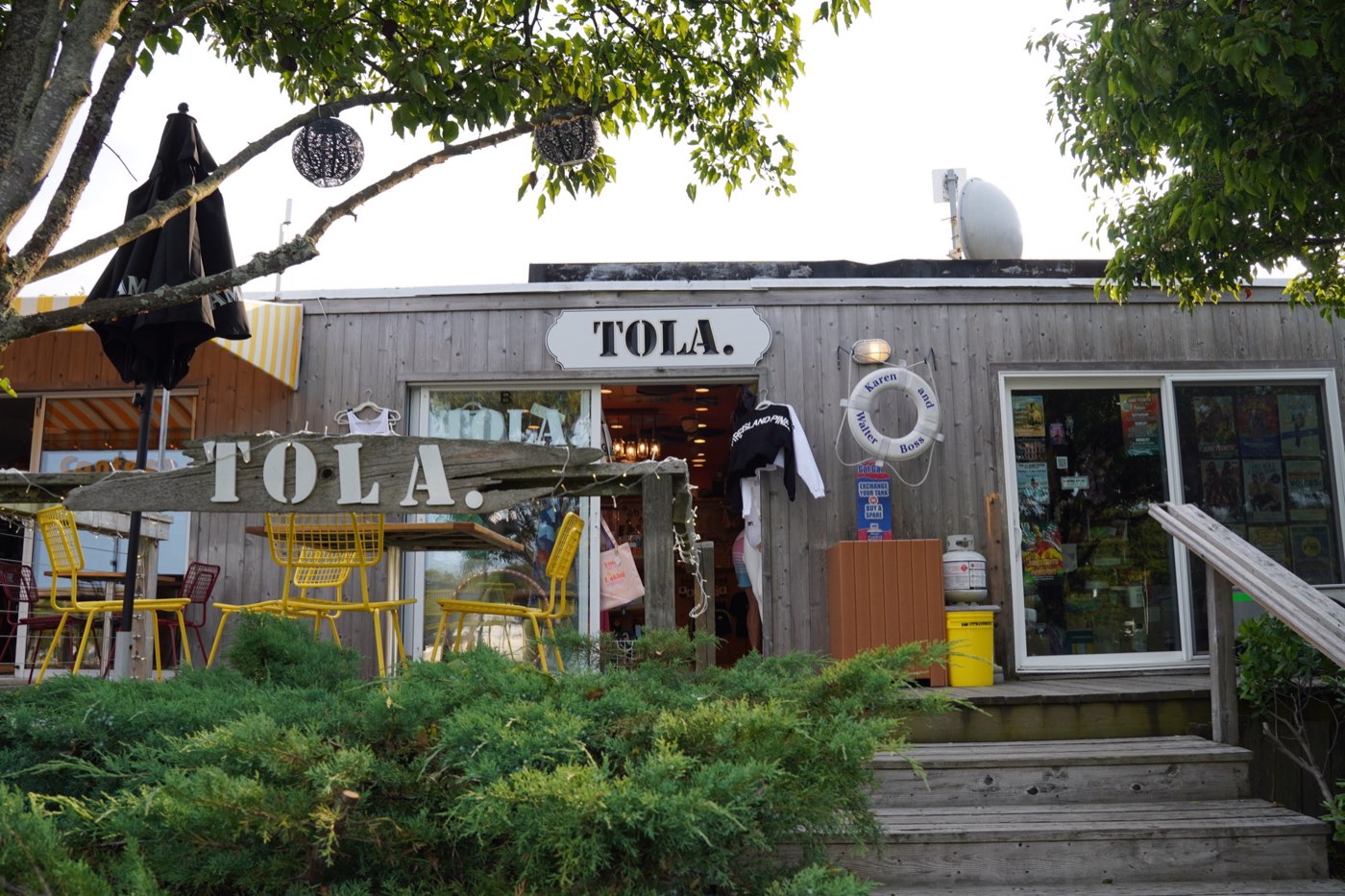 TOLA. shop in Fire Island Pines, weathered-wood storefront with the TOLA. sign and yellow cafe chairs.