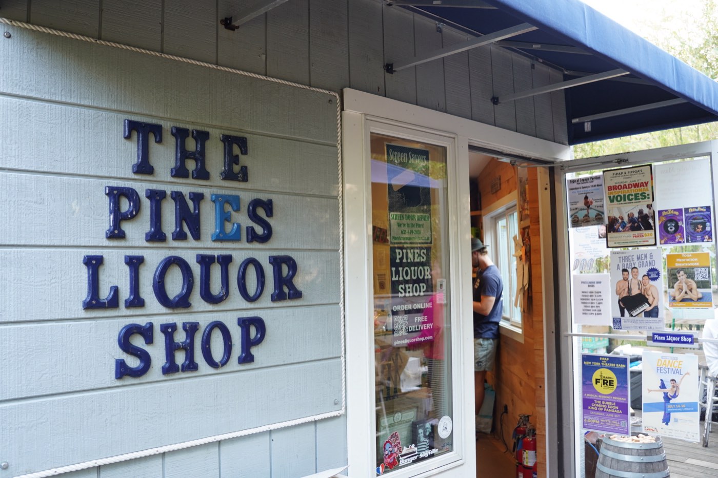 The Pines Liquor Shop storefront, blue lettering on grey clapboard with a navy awning.