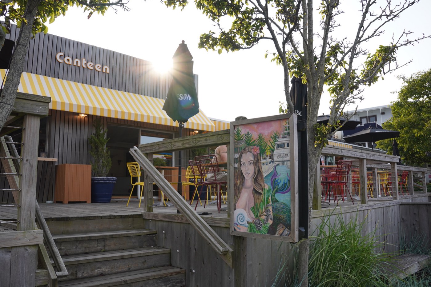 Canteen in Fire Island Pines at golden hour, yellow-striped awning and outdoor deck seating.